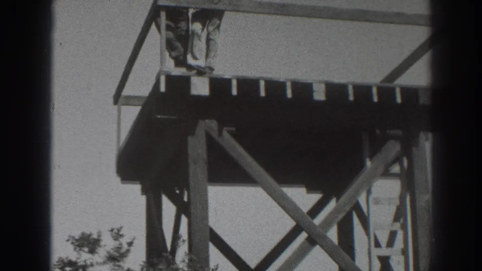 A person stands near the top platform of the Sacramento observation tower, partly framed by railing, braces, trees, and bright sky.