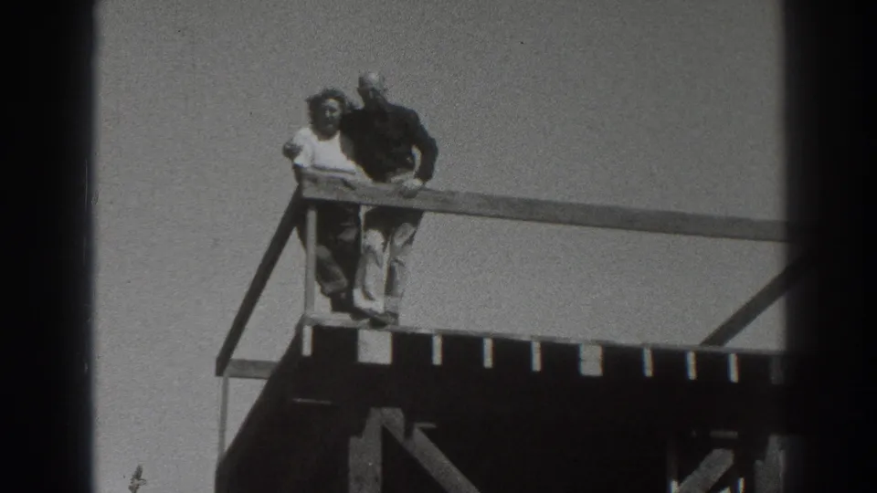 A man and woman face outward from the elevated wooden structure, with diagonal bracing visible beneath the deck.