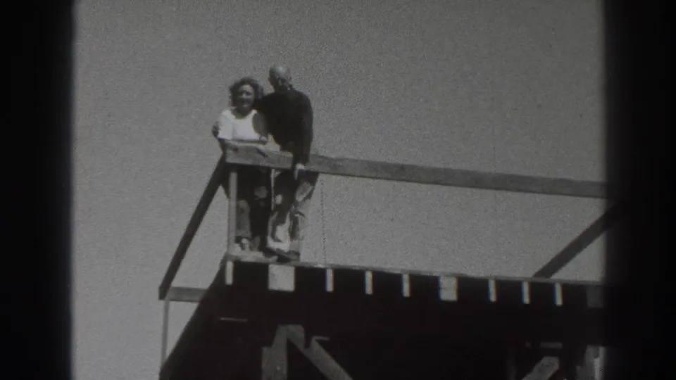 The woman stands in front at the railing while the man remains close behind on the raised wooden platform.