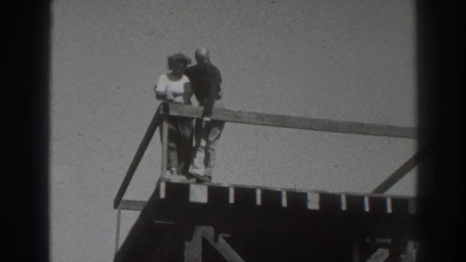 In 1937 Sacramento footage, a couple stands near the corner of a wooden platform, looking outward from an elevated railing.