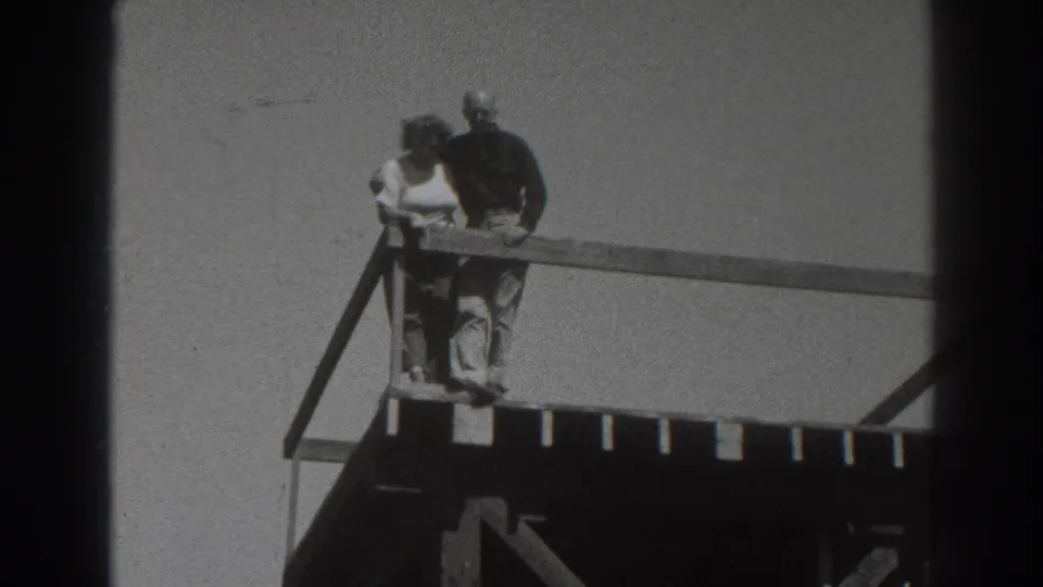 The couple remains at the railing of an elevated wooden structure in the Sacramento home-movie footage, framed against open sky.