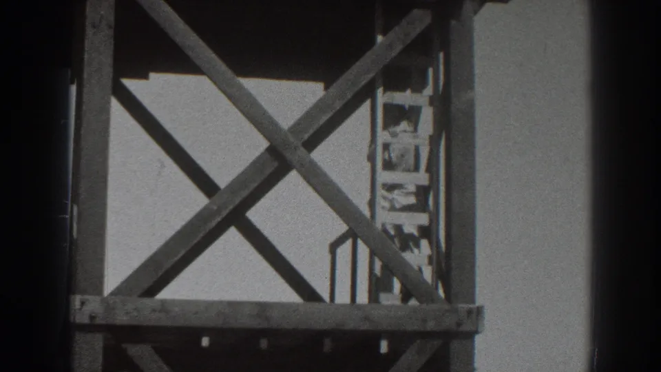 1937 Sacramento 8mm frame showing a man climbing or standing on a ladder inside a tall wooden scaffold with X-shaped braces.
