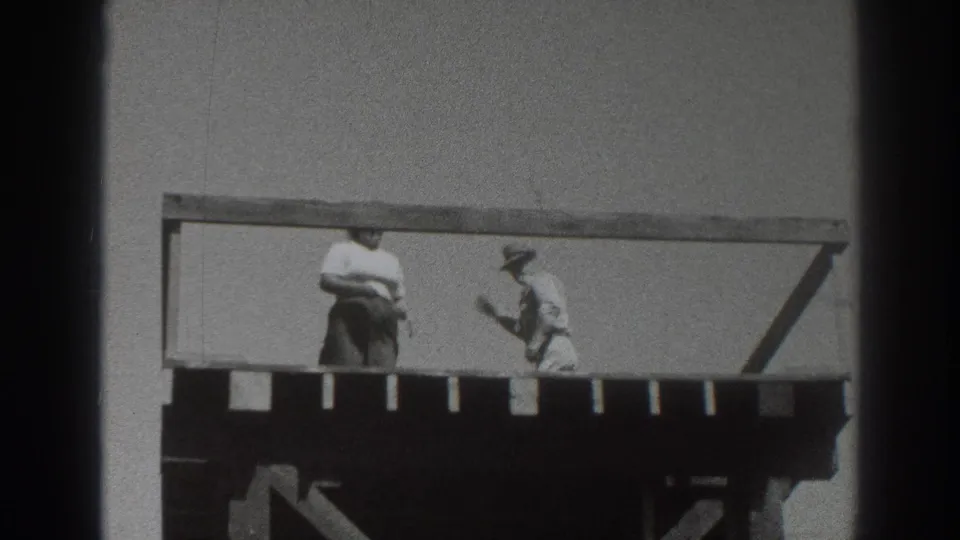1937 Sacramento frame showing two adults on a raised wooden deck, one near the center and one in a hat by the railing.
