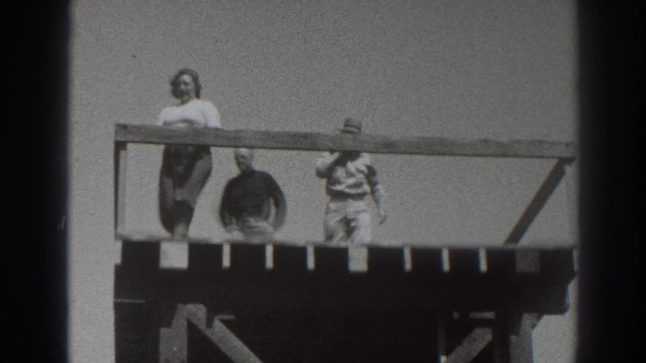 1937 Sacramento home-movie frame showing a woman in a light top and dark skirt near a hat-wearing man on the raised wooden deck.