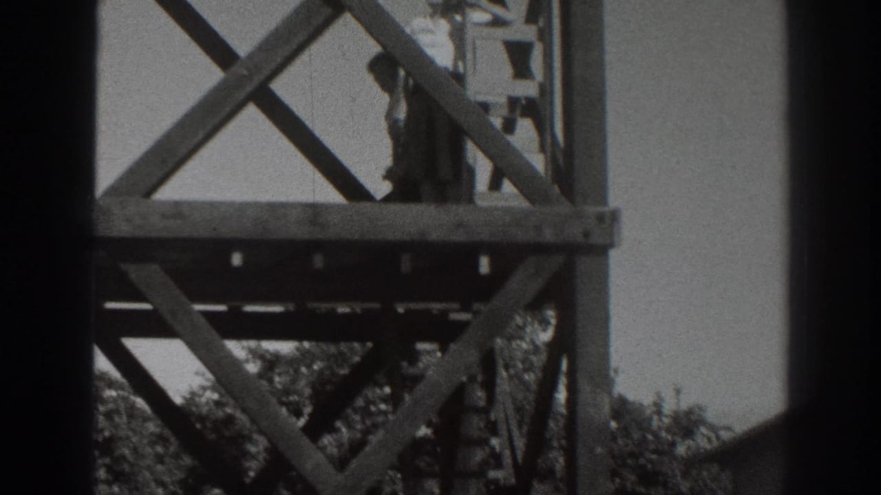 A person on a lower wooden platform near a ladder and cross-bracing, seen in black-and-white 8mm footage.