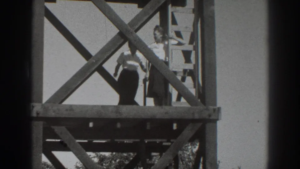 A woman in a light top stands on a lower wooden platform beside a ladder and diagonal braces in Sacramento, 1937.