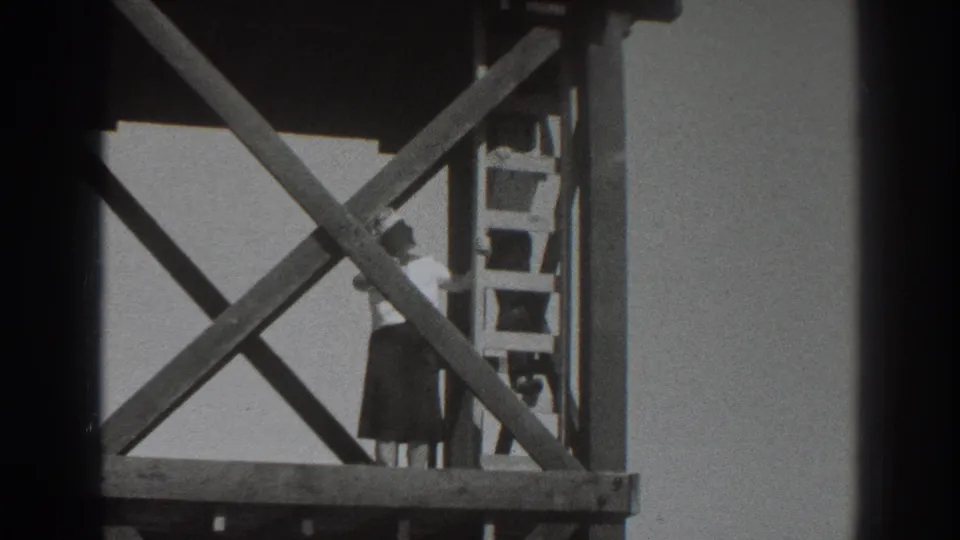 A lower view of the scaffold shows the woman near the ladder, partly obscured by heavy wooden cross-bracing.