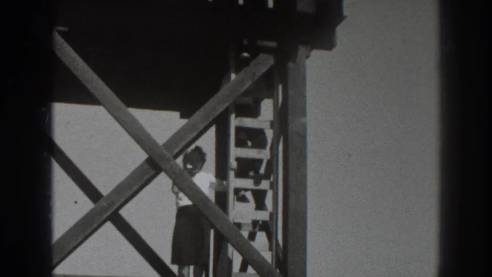 The final frame shows the woman beside the ladder beneath the platform, with strong diagonal wood beams across the view.