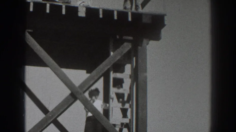 1937 Sacramento home-movie frame showing a man on a ladder below a timber platform with diagonal bracing and a worker partly visible at the top.