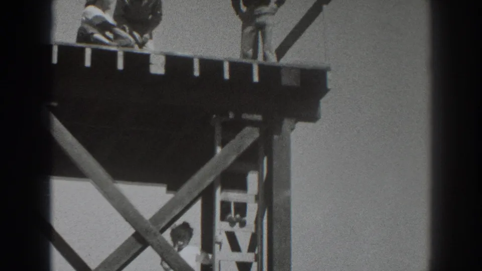 1937 Sacramento frame showing the timber platform from below, with a man near the ladder and two workers cropped along the upper deck.