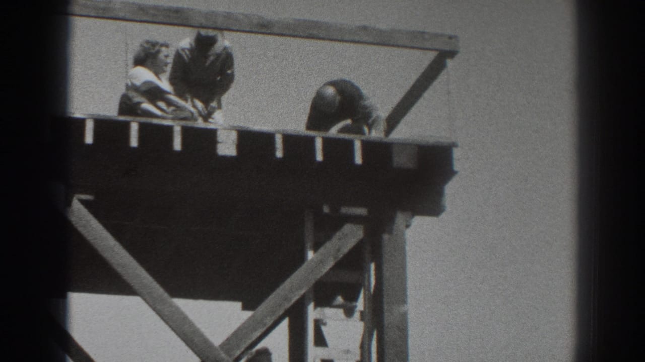 1937 Sacramento home-movie frame with two men working near the rail of an elevated timber platform and another figure partly obscured underneath.