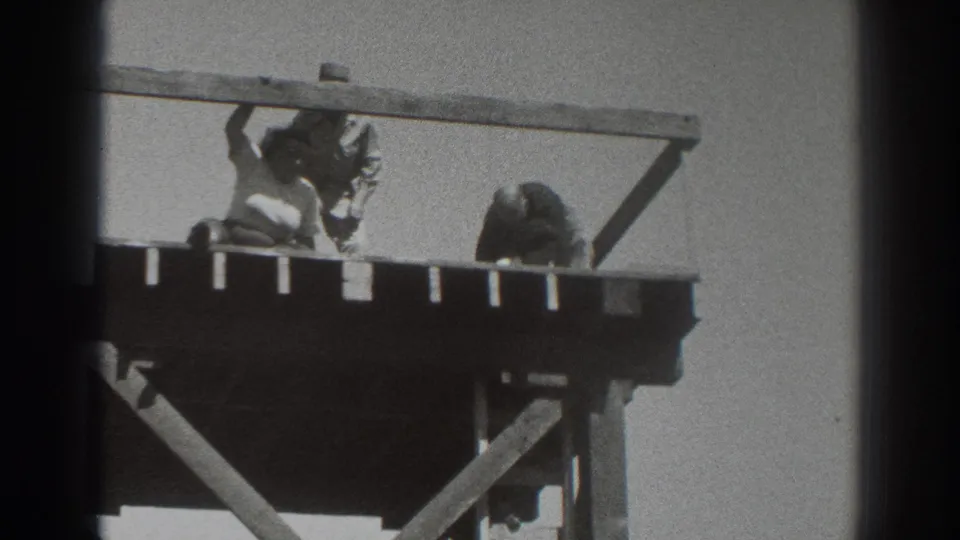 1937 Sacramento frame showing three men clustered on an elevated wooden platform, with one near the rail, one bending, and the tower braces below.