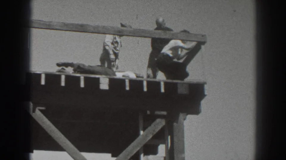 1937 Sacramento home-movie frame showing adults on a wooden tower platform, including a prone person and two standing figures.