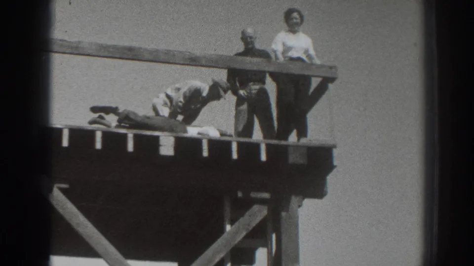 1937 Sacramento footage shows a woman in a light blouse and two men near a prone person on a high wooden platform.