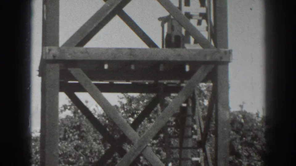 1937 Sacramento home-movie frame showing a wooden observation tower with cross-bracing, ladder rungs, trees, and dark film borders.