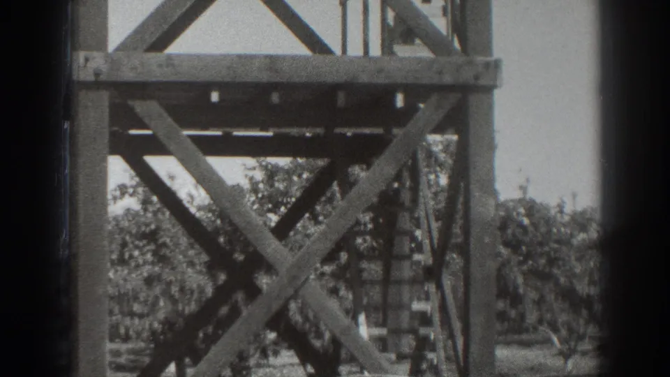 1937 Sacramento 8mm frame focused on the cross-braced lower portion of the wooden observation tower with trees behind it.