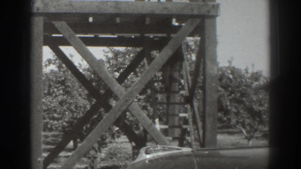 1937 Sacramento frame showing the tower supports and ladder with trees behind and the partial roofline of a vehicle at lower right.