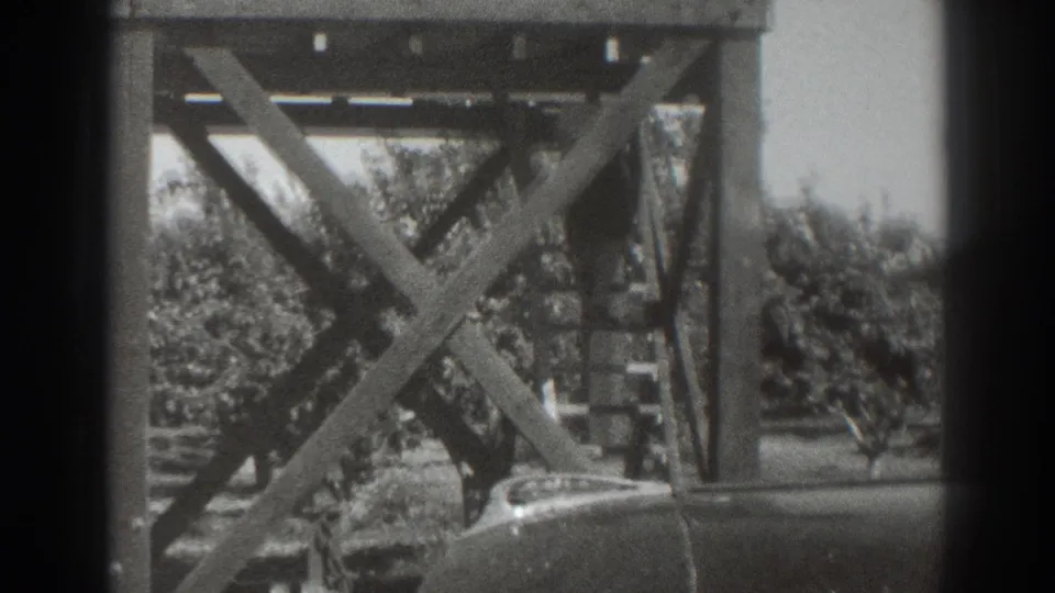 1937 Sacramento home-movie frame showing a timber stair structure, orchard trees, and the rounded hood of a parked car.
