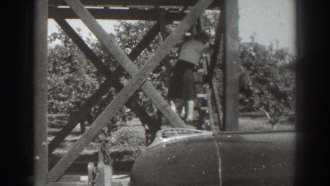 1937 Sacramento home-movie frame of a woman descending a steep exterior wooden stair near orchard trees and a parked car.