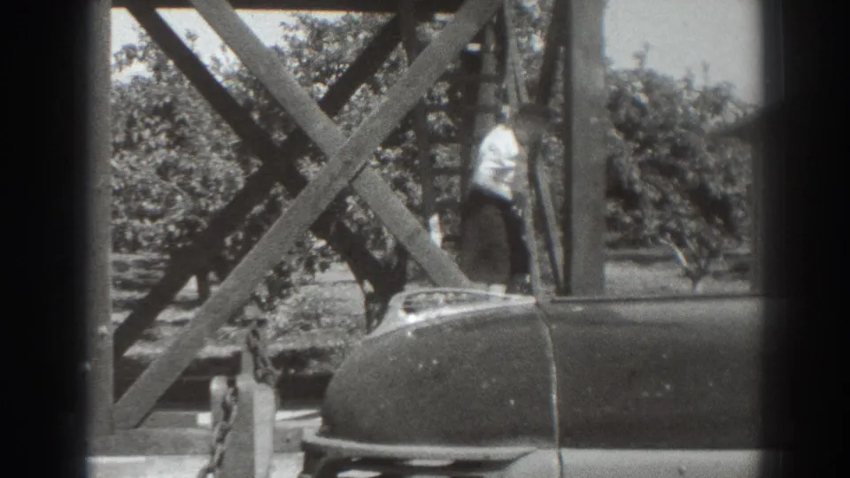 1937 Sacramento frame showing a woman at the lower part of a wooden staircase, with orchard trees and a parked car in view.