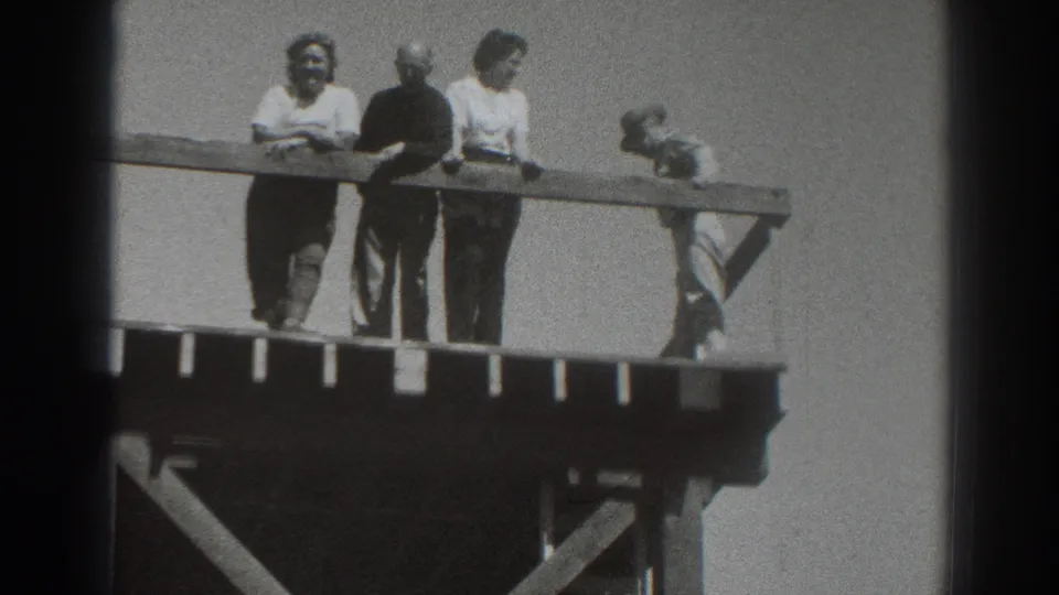 In 1937 Sacramento footage, four adults stand on a wooden observation platform while leaning near the rail in windy conditions.