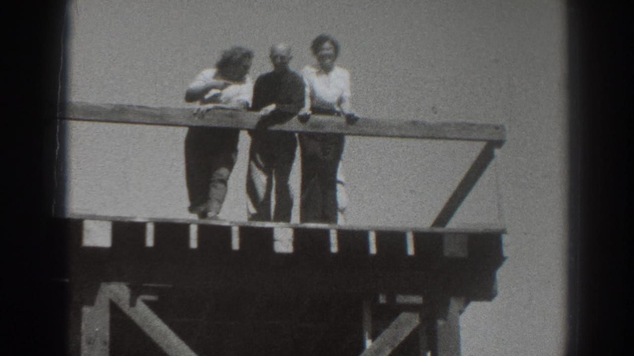 Adults in 1937 Sacramento home-movie footage lean on a wooden railing, with wind affecting hair and clothing.