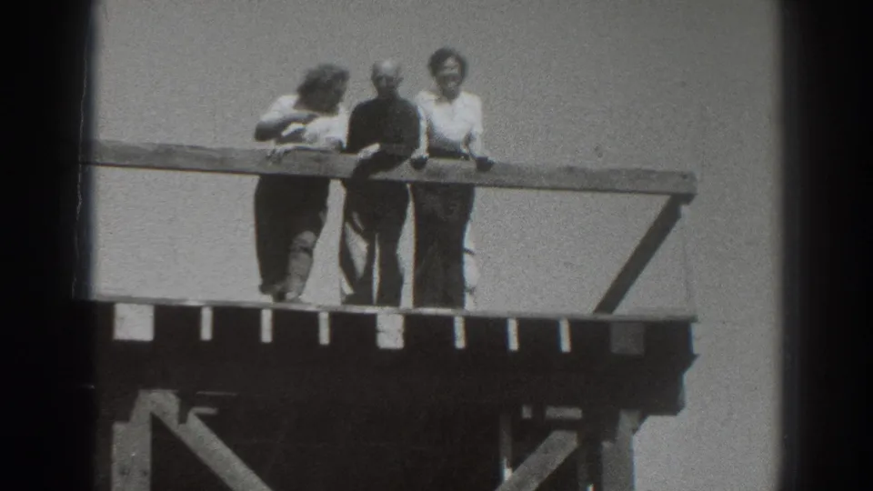 Adults in 1937 Sacramento home-movie footage lean on a wooden railing, with wind affecting hair and clothing.