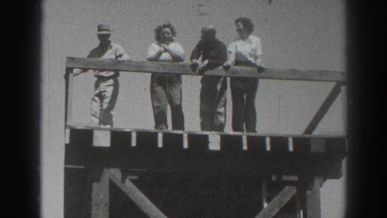 Four adults stand behind a wooden railing on an elevated outdoor platform.