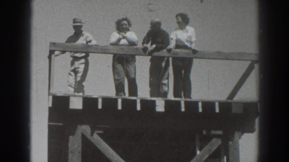 In 1937 Sacramento home-movie footage, four adults stand on a wooden platform under a bright sky, with a man in a hat at left.