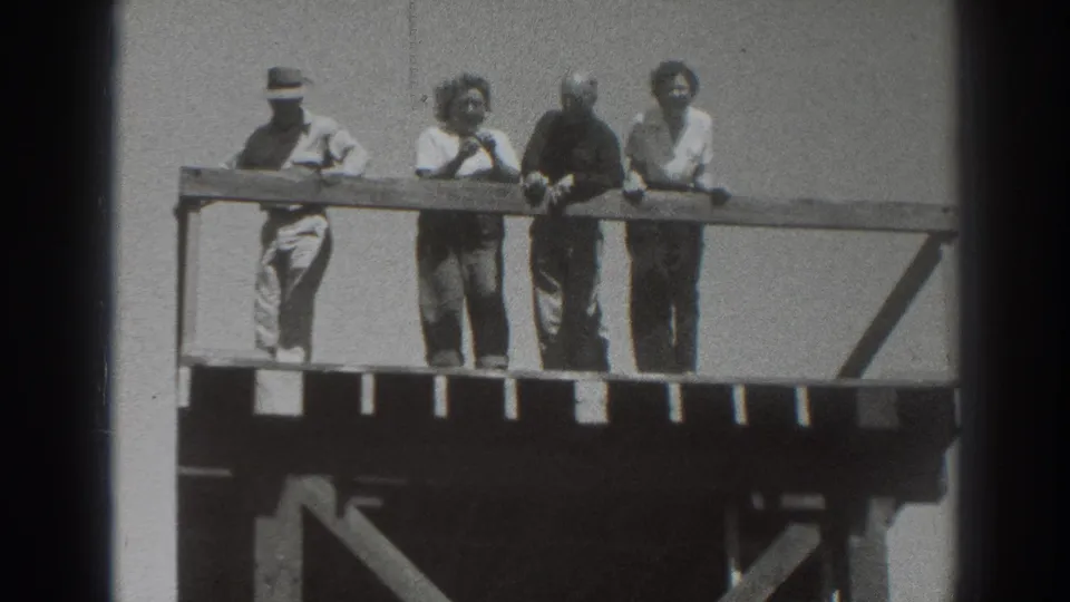 Four adults remain at the railing on an elevated wooden platform in Sacramento, with the left figure in a hat and others facing outward.