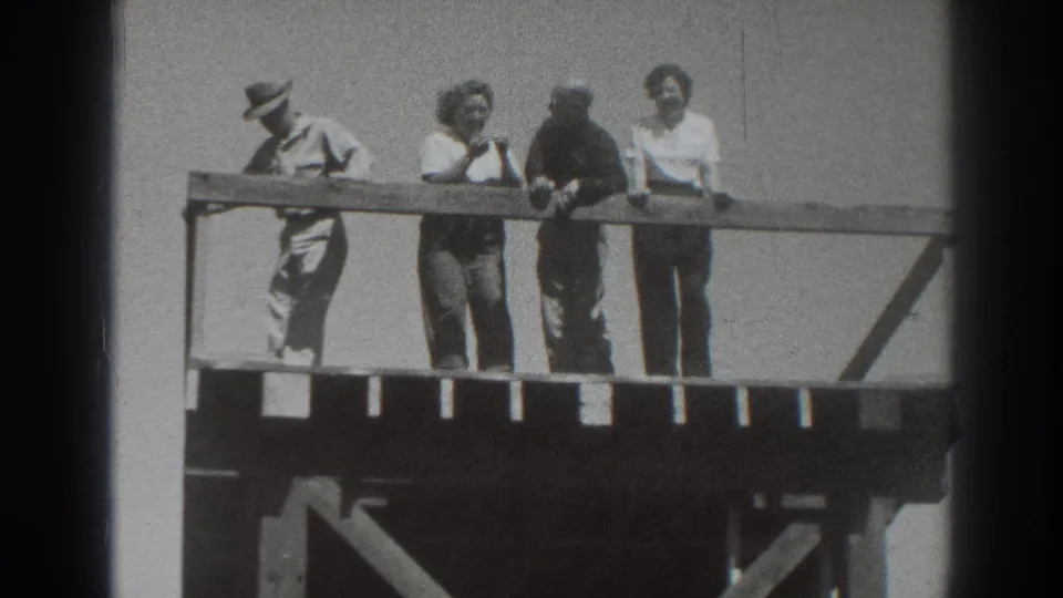 On the wooden platform, the man at left bends forward while three other adults stand near the railing in bright 1937 Sacramento footage.