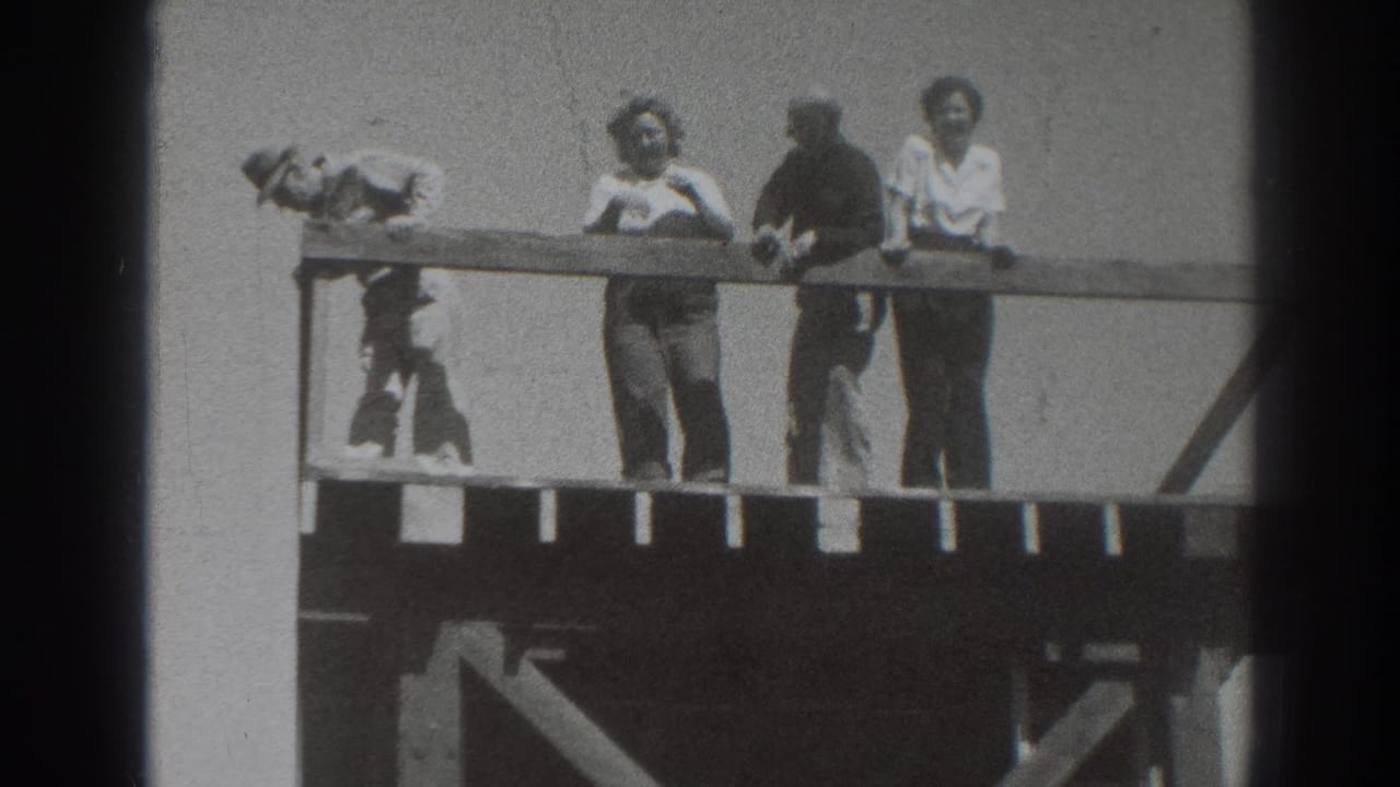 The left figure bends low beside the railing as three adults continue standing on the elevated wooden platform in Sacramento home-movie footage.