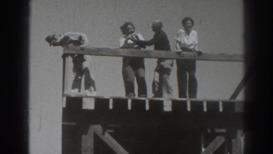 In 1937 Sacramento home-movie footage, several adults gather on a wooden deck as one leans far over the rail.