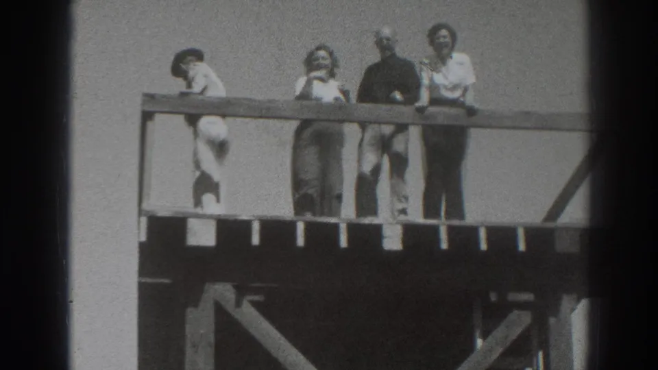 Four adults appear along a wooden deck railing in Sacramento, with one person bent forward and others watching or smiling.