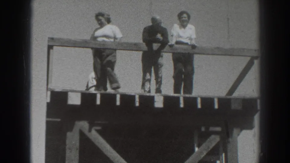 Three adults remain at the railing of a wooden deck in Sacramento, framed by open sky and visible 8mm film edges.