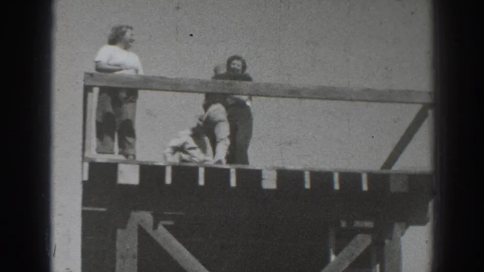 1937 Sacramento home-movie frame showing two people near an elevated wooden platform or railing, with soft focus and heavy film grain.