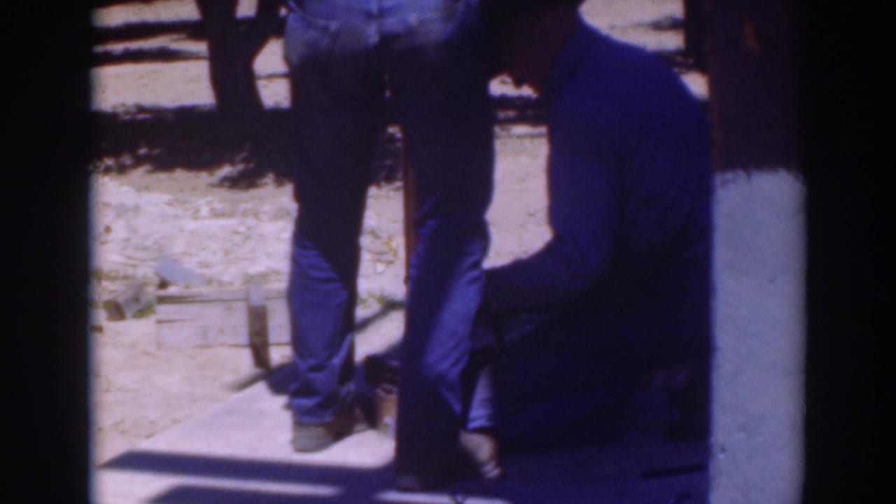 Home-movie frame from Sacramento in 1937 showing two men close to a low board and wooden work area on dry ground.