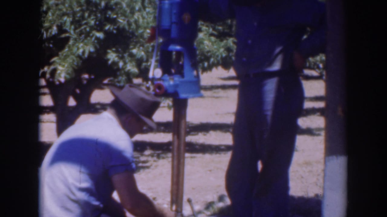 Crouching man works at the pole base while a standing man remains beside the mounted tool.