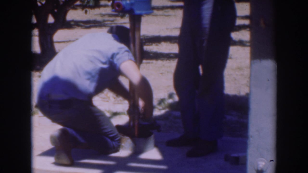 Near the end of the clip, the worker kneels by the pole footing in the 1937 Sacramento orchard as a second man stands next to him.