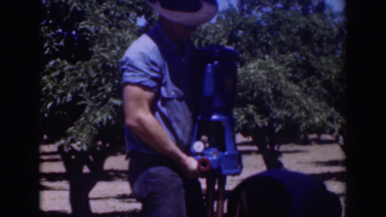 A man wearing a brimmed hat stands next to the blue pump in the Sacramento outdoor setting, with trees visible behind him.