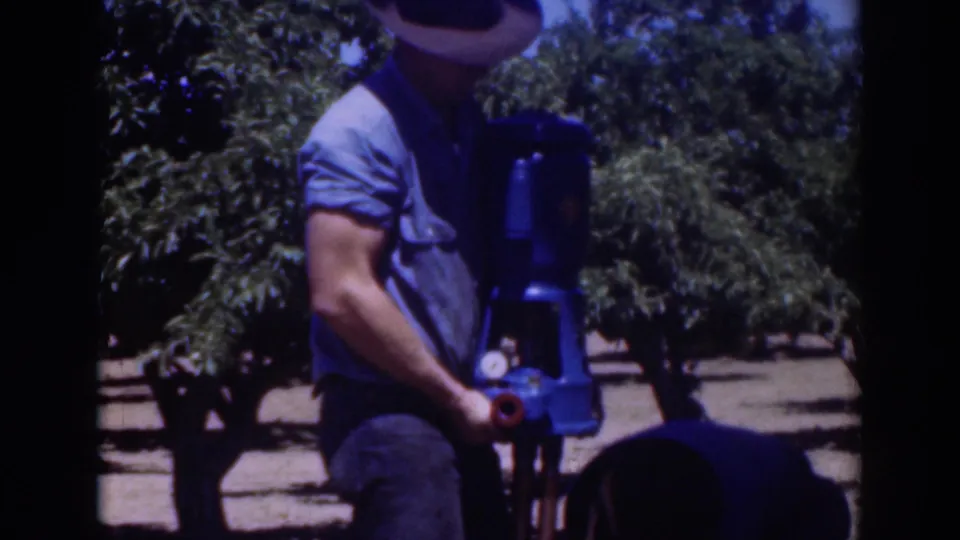 A man wearing a brimmed hat stands next to the blue pump in the Sacramento outdoor setting, with trees visible behind him.