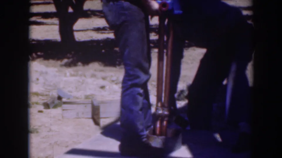 Two adult men in Sacramento, California, stand close to a vertical hand tool and blue object on dry ground in 1937 home-movie footage.