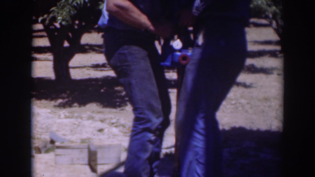 In this 1937 Sacramento frame, two men lean into a close outdoor task around a blue object and vertical tool on dry soil.