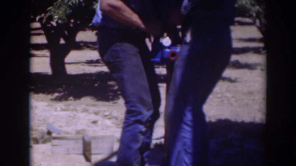 In this 1937 Sacramento frame, two men lean into a close outdoor task around a blue object and vertical tool on dry soil.