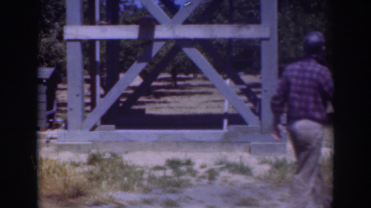 The man moves toward the right edge of the 1937 Sacramento frame, with a pale wooden structure and trees behind him.