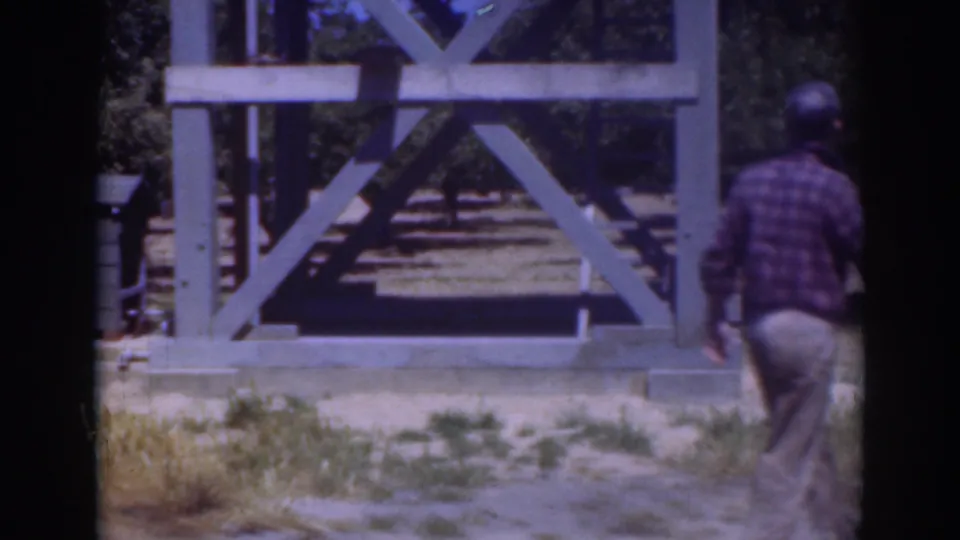 The man moves toward the right edge of the 1937 Sacramento frame, with a pale wooden structure and trees behind him.