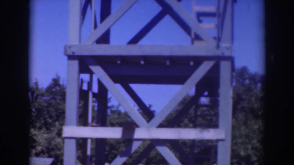 1937 Sacramento frame showing the X-braced blue wooden tower and ladder area with trees in the background.