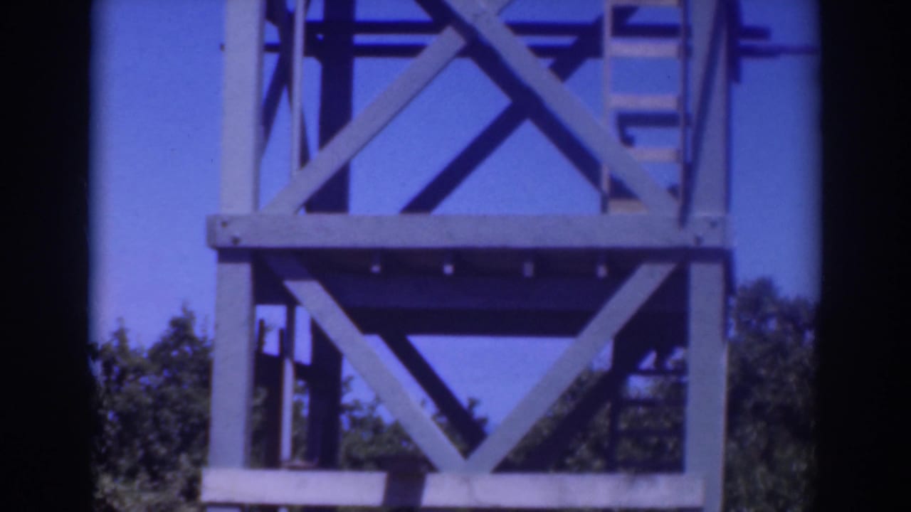 Metal tower with cross-bracing against blue sky and tree tops below.