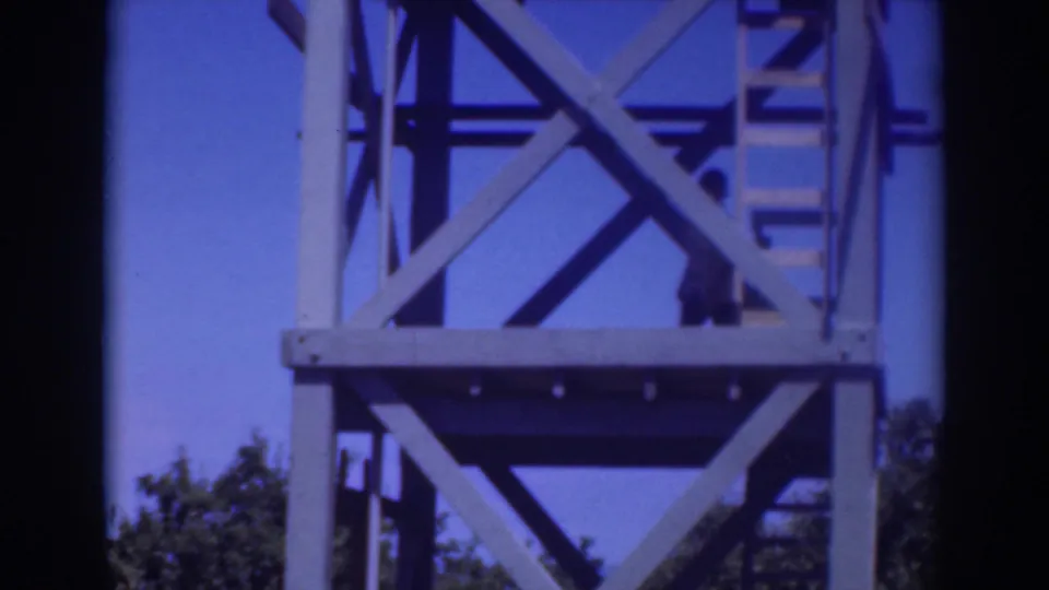 1937 Sacramento 8mm frame with a person partly visible on the tower ladder beside steel bracing and a clear blue sky.