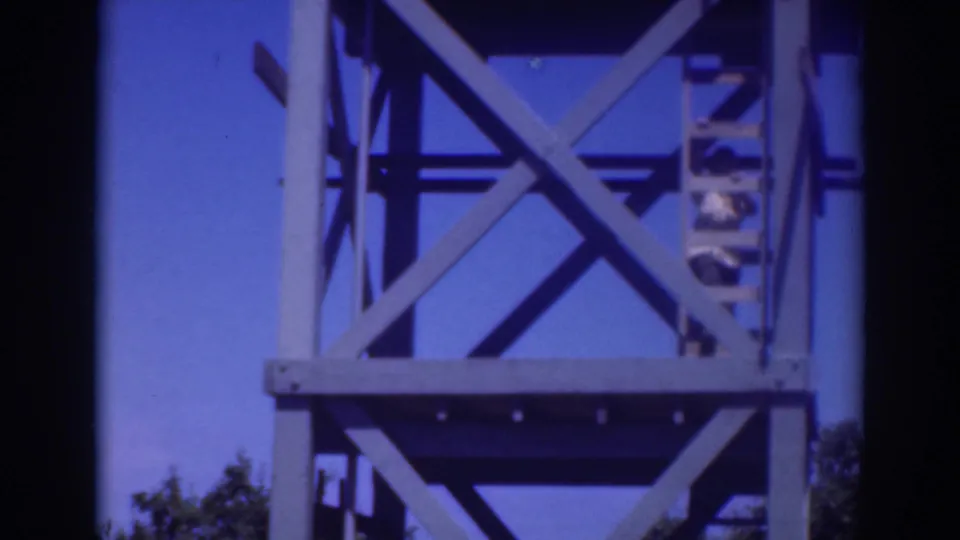 1937 Sacramento 8mm frame showing the tower ladder and cross-braced structure, with the climber partly obscured on the right side.